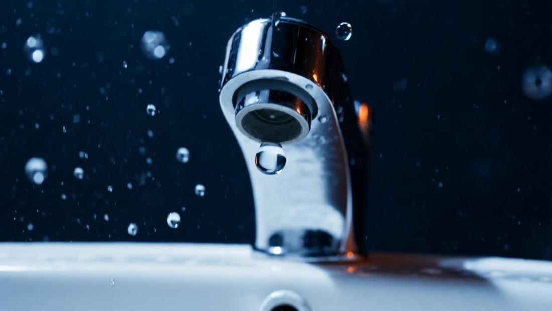 A chrome tap over a white basin with a drop forming